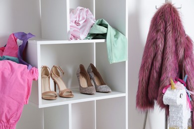 Photo of Shelving unit with different footwear and clothes indoors. Shoe storage