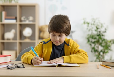 Photo of Cute little boy doing homework at table indoors