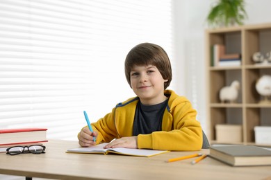 Photo of Cute little boy doing homework at table indoors