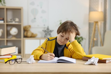 Photo of Tired little boy doing homework at table indoors