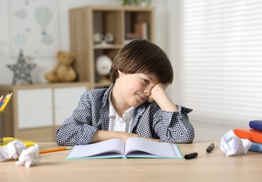 Photo of Tired little boy doing homework at table indoors