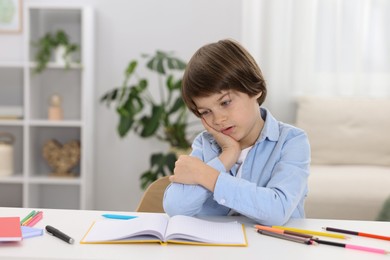 Photo of Tired little boy doing homework at table indoors