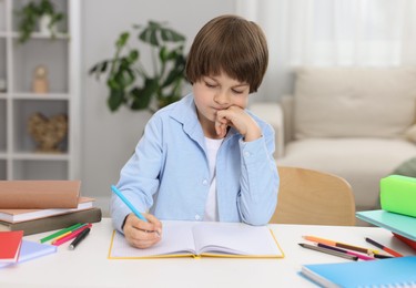 Photo of Cute little boy doing homework at table indoors
