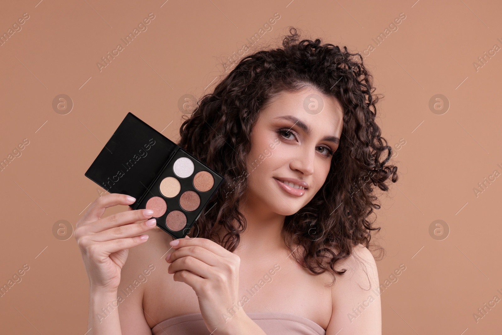 Smiling woman with eyeshadow palette on beige background Photo of Smiling woman with eyeshadow palette on beige background