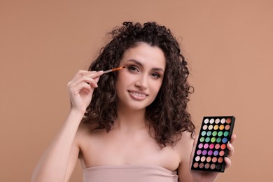Photo of Smiling woman with eyeshadow palette and brush applying makeup on beige background