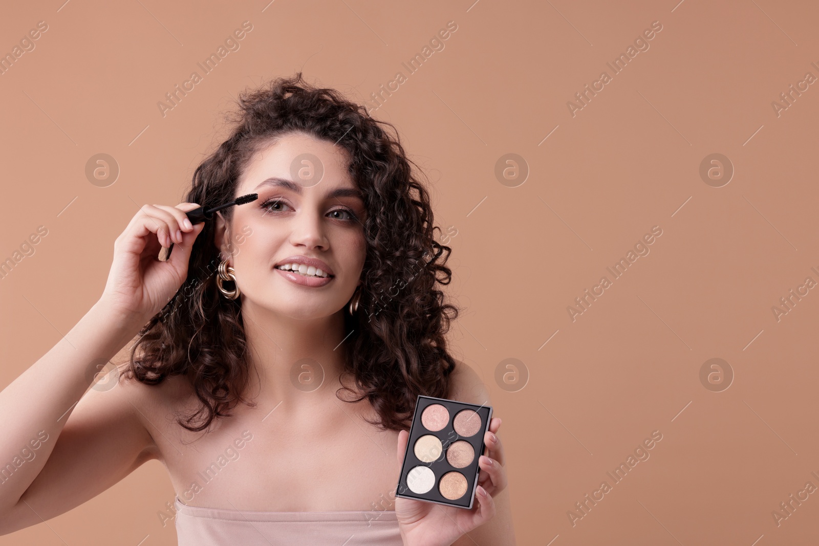 Smiling woman with eyeshadow palette and brush applying makeup on beige background. Space for text Photo of Smiling woman with eyeshadow palette and brush applying makeup on beige background. Space for text
