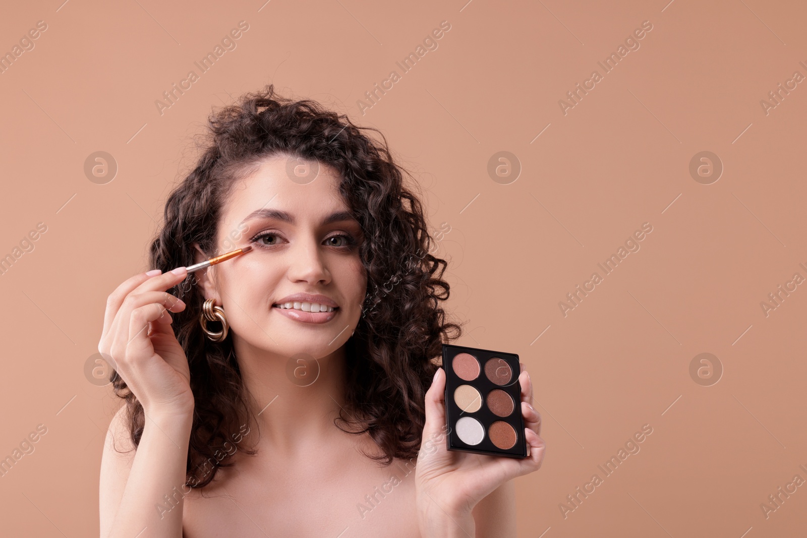 Smiling woman with eyeshadow palette and brush applying makeup on beige background. Space for text Photo of Smiling woman with eyeshadow palette and brush applying makeup on beige background. Space for text