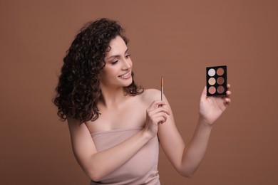 Photo of Smiling woman with eyeshadow palette and brush on brown background