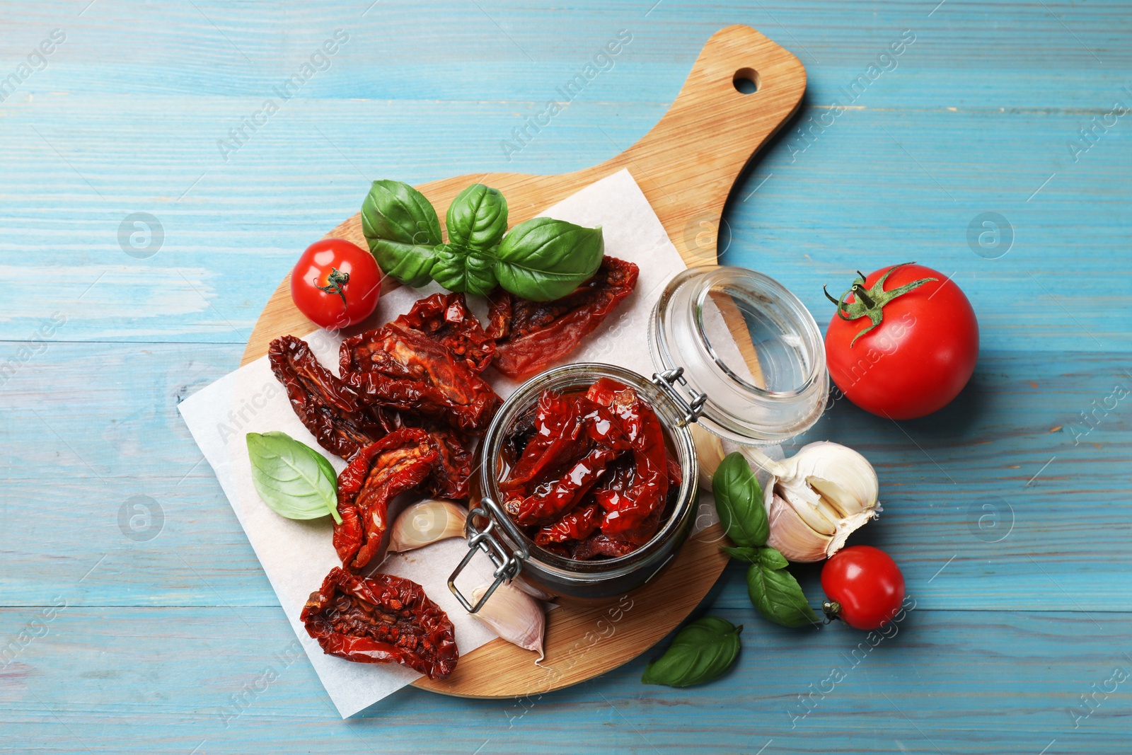 Delicious sun dried tomatoes in glass jar, fresh vegetables and spices on light blue wooden table, flat lay Photo of Delicious sun dried tomatoes in glass jar, fresh vegetables and spices on light blue wooden table, flat lay