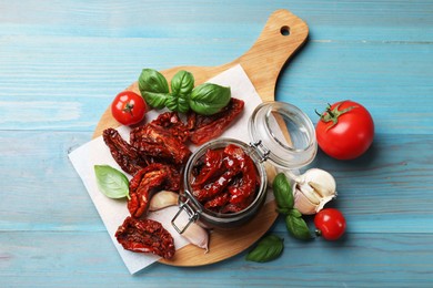 Photo of Delicious sun dried tomatoes in glass jar, fresh vegetables and spices on light blue wooden table, flat lay