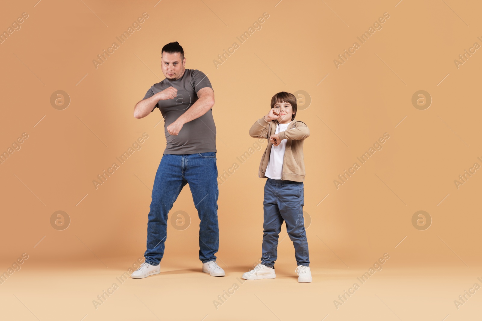 Father and his son dancing together on beige background Photo of Father and his son dancing together on beige background