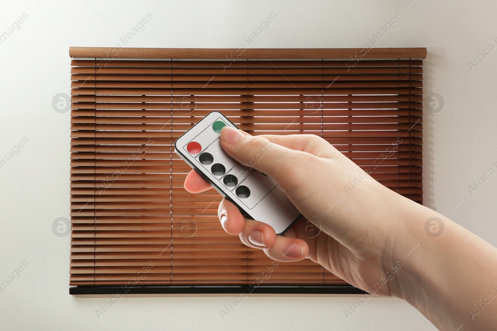 Woman using remote to control blinds in room, closeup Image of Woman using remote to control blinds in room, closeup