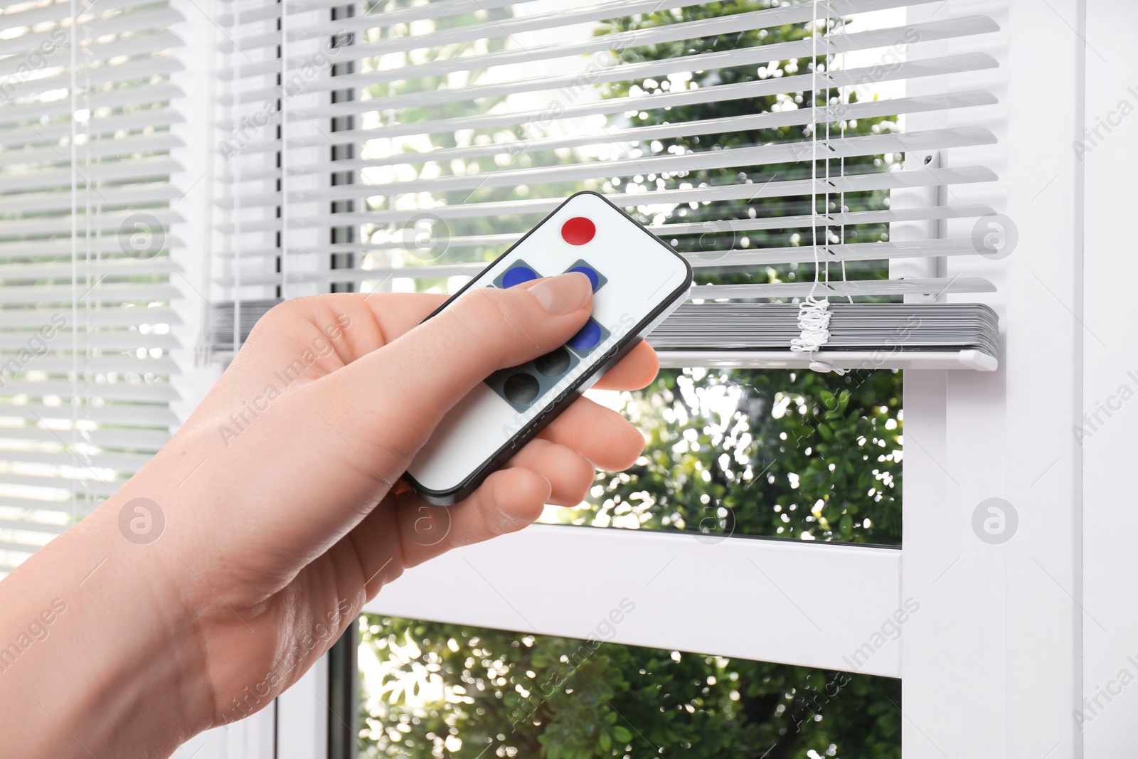 Woman using remote to control blinds in room, closeup Image of Woman using remote to control blinds in room, closeup