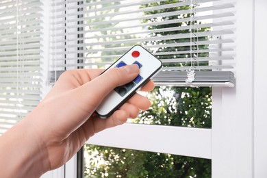 Image of Woman using remote to control blinds in room, closeup