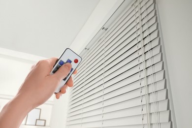 Image of Woman using remote to control blinds in room, closeup