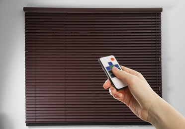Image of Woman using remote to control blinds in room, closeup