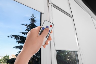 Image of Woman using remote to control blinds in room, closeup