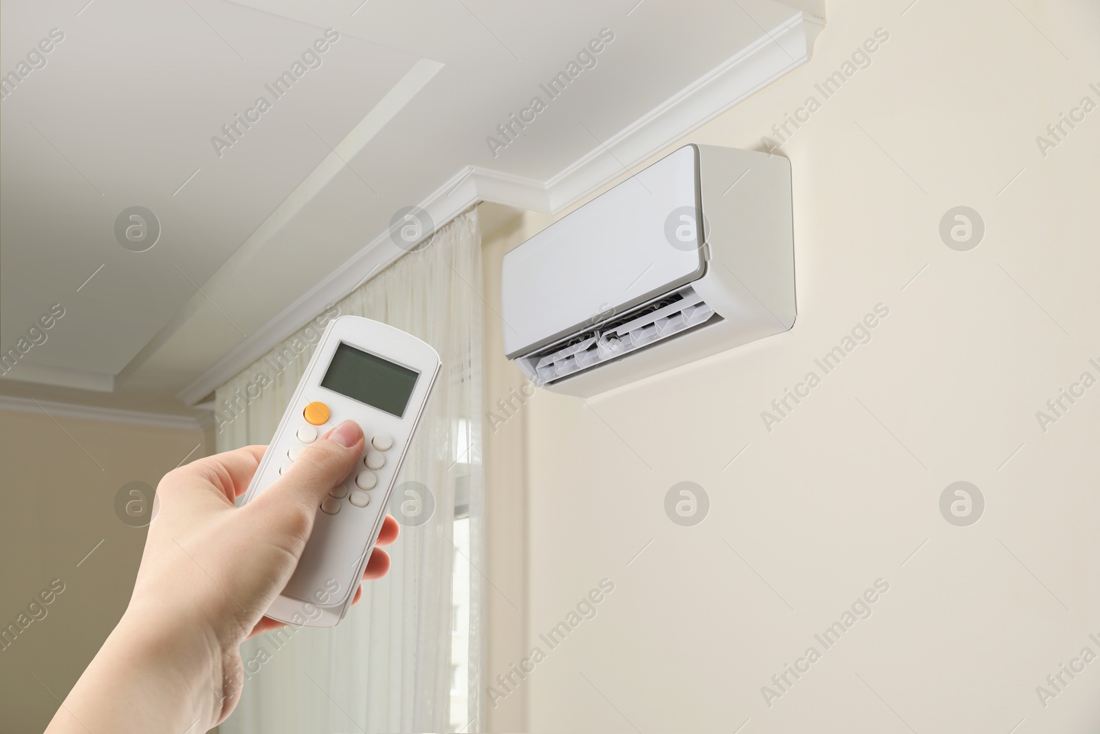 Woman using remote to control air conditioner in room, closeup Image of Woman using remote to control air conditioner in room, closeup