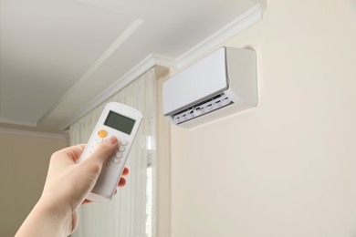 Image of Woman using remote to control air conditioner in room, closeup
