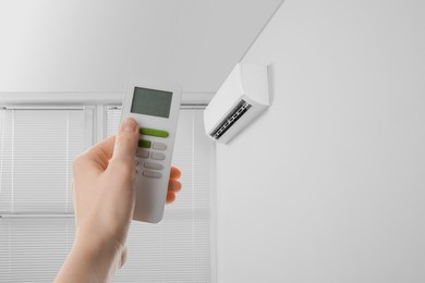 Image of Woman using remote to control air conditioner in room, closeup