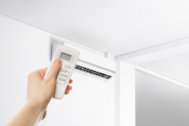 Image of Woman using remote to control air conditioner in room, closeup