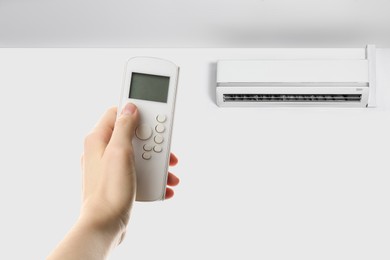 Image of Woman using remote to control air conditioner in room, closeup