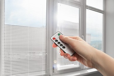 Image of Woman using remote to control blinds in room, closeup
