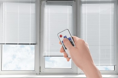 Image of Woman using remote to control blinds in room, closeup