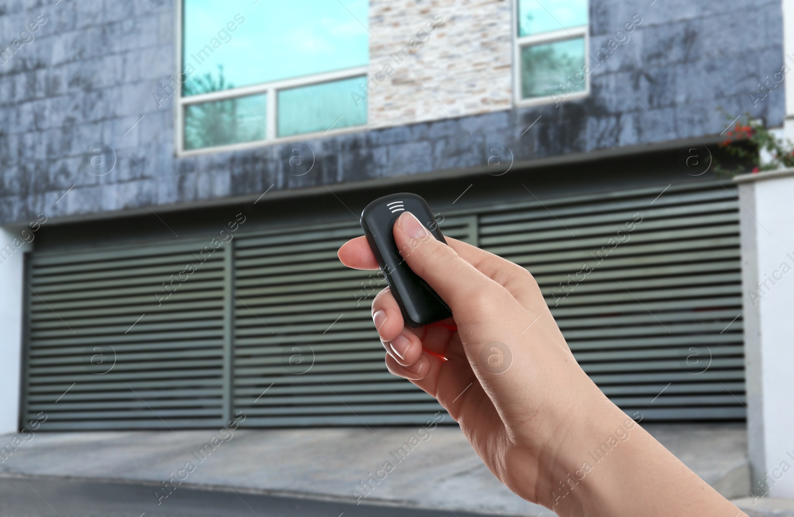 Woman using remote to control roller shutters outdoors, closeup Image of Woman using remote to control roller shutters outdoors, closeup