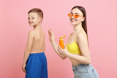 Photo of Mother applying sun protection cream onto her son's skin on pink background
