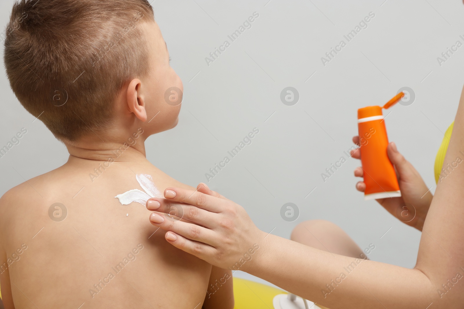 Photo of Mother applying sun protection cream onto her son's skin on light grey background, closeup