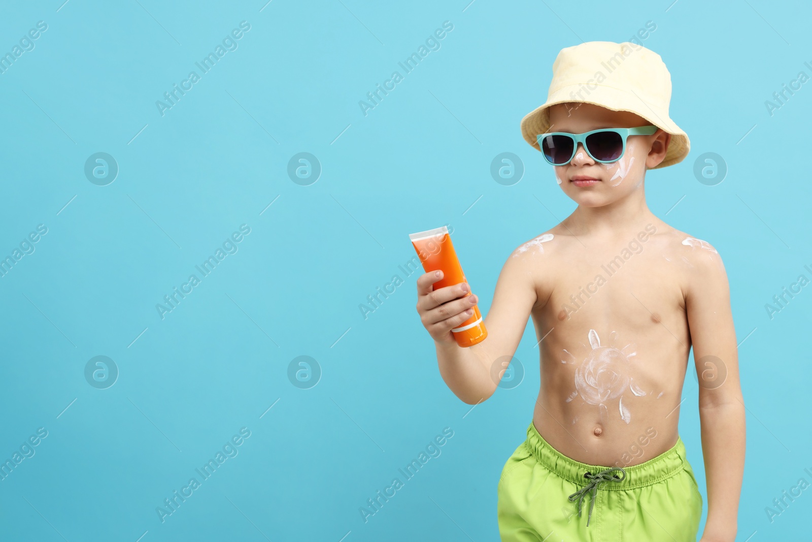Little boy with tube of sun protection cream on light blue background, space for text Photo of Little boy with tube of sun protection cream on light blue background, space for text