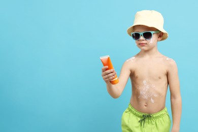 Photo of Little boy with tube of sun protection cream on light blue background, space for text