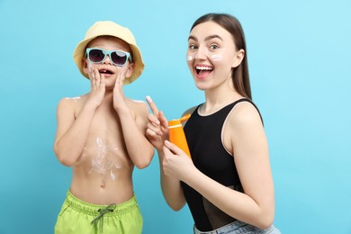 Photo of Emotional mother with sun protection cream and her son on light blue background