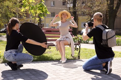 Photo of Professional photographers with reflector and camera near model during shooting outdoors on sunny day