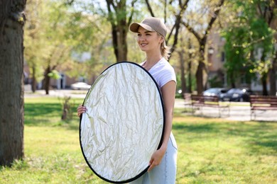 Photo of Woman with reflector outdoors on sunny day. Photography equipment
