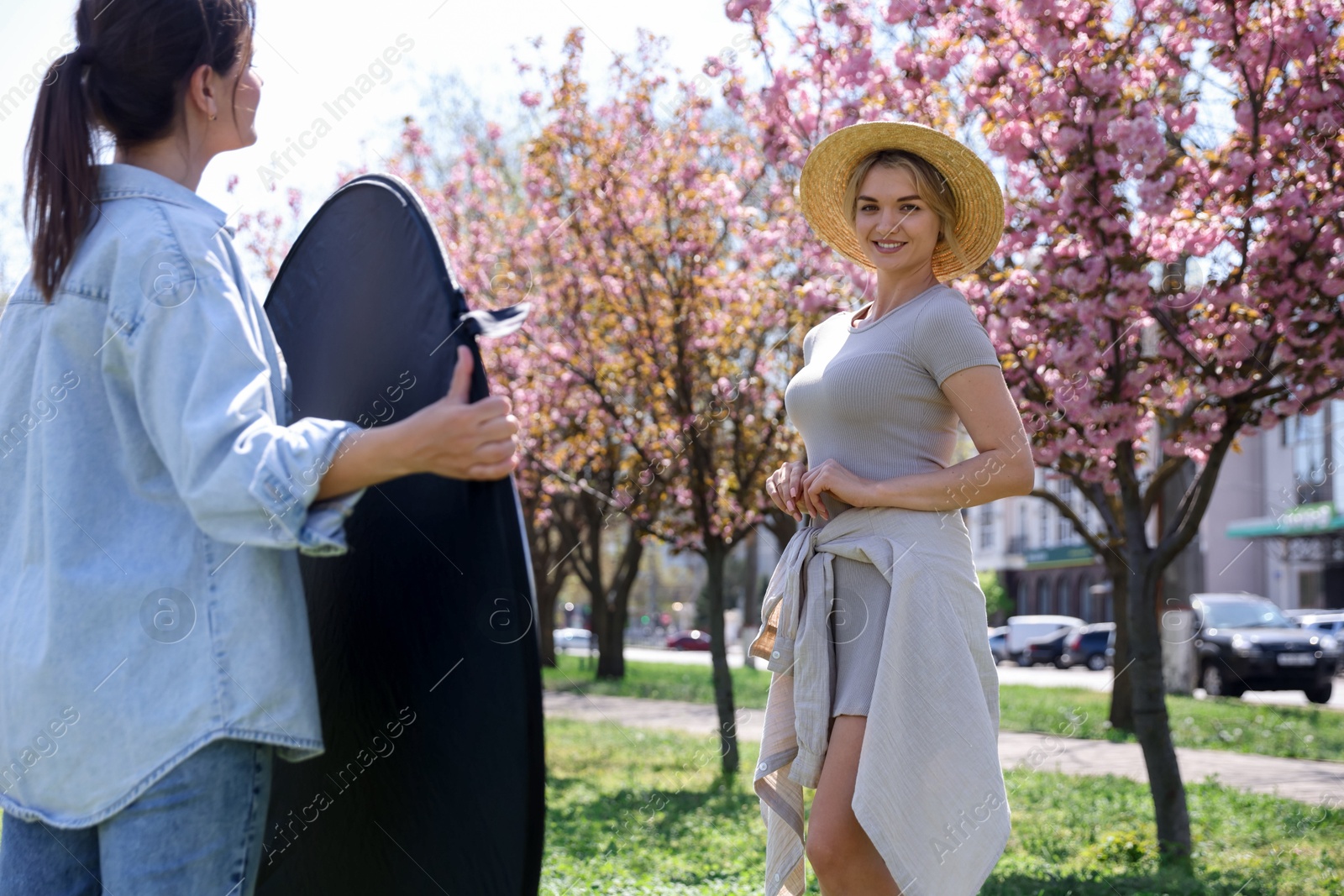 Professional photographer with reflector near model during shooting outdoors on sunny day Photo of Professional photographer with reflector near model during shooting outdoors on sunny day