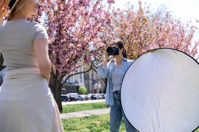 Photo of Professional photographer with camera and reflector near model during shooting outdoors on sunny day