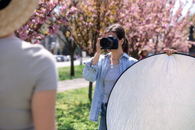 Photo of Professional photographer with camera and reflector near model during shooting outdoors on sunny day