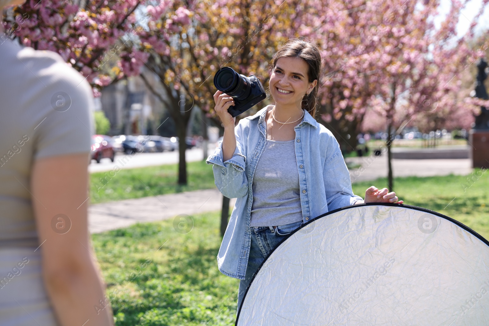 Professional photographer with camera and reflector near model during shooting outdoors on sunny day Photo of Professional photographer with camera and reflector near model during shooting outdoors on sunny day