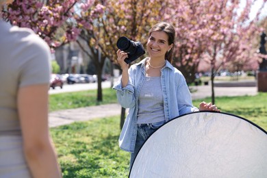 Photo of Professional photographer with camera and reflector near model during shooting outdoors on sunny day