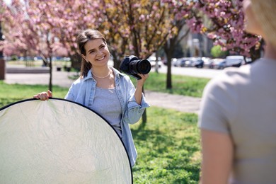 Photo of Professional photographer with camera and reflector near model during shooting outdoors on sunny day
