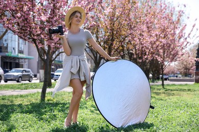 Photo of Woman with camera and reflector outdoors on sunny day. Photography equipment