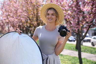 Photo of Woman with camera and reflector outdoors on sunny day. Photography equipment