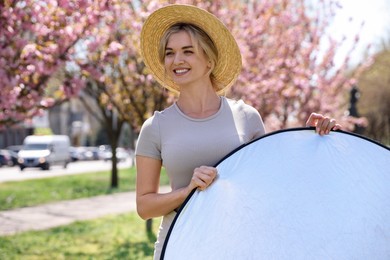 Photo of Woman with reflector outdoors on sunny day. Photography equipment