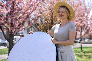 Photo of Woman with reflector outdoors on sunny day. Photography equipment