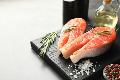 Photo of Seafood. Raw salmon steaks, rosemary and spices on grey table, closeup. Space for text
