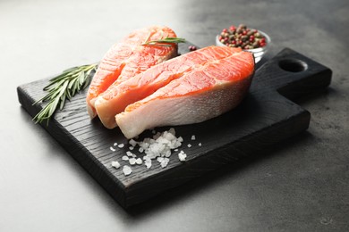 Photo of Seafood. Raw salmon steaks, rosemary and spices on grey table, closeup
