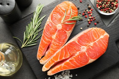 Photo of Seafood. Raw salmon steaks, rosemary and spices on grey table, flat lay