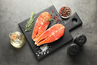 Photo of Seafood. Raw salmon steaks, rosemary and spices on grey table, flat lay